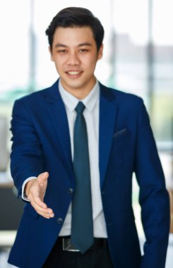 Seçkin takım elbiseli, etkin erkek girişimci ofiste el sıkışmak için elini uzatarak kameraya bakıyor.