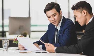 Memnuniyetle Asyalı erkek yöneticiler masada oturup birlikte tablet kullanırken işyerindeki yeni projeden bahsediyorlar.