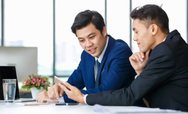 Memnuniyetle Asyalı erkek yöneticiler masada oturup birlikte tablet kullanırken işyerindeki yeni projeden bahsediyorlar.