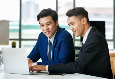 Olumlu Asyalı işadamları yeni proje üzerinde çalışırken masada oturup ağlara bakıyorlar.