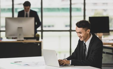 Gülümseyen etnik erkek girişimci netbook 'ta yazıyor ve iş yerinde tanınmayan erkek meslektaşıyla proje üzerinde çalışıyor.