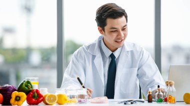 Hastanede meyve ve vitaminlerle masada otururken gülümseyen ve not alan neşeli Asyalı tıp doktoru.