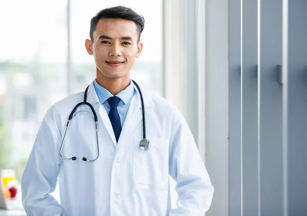 Üniformalı Neşeli Genç Yakışıklı Asyalı Erkek Doktor Steteskopu Klinikte Duruyor — Stok fotoğraf