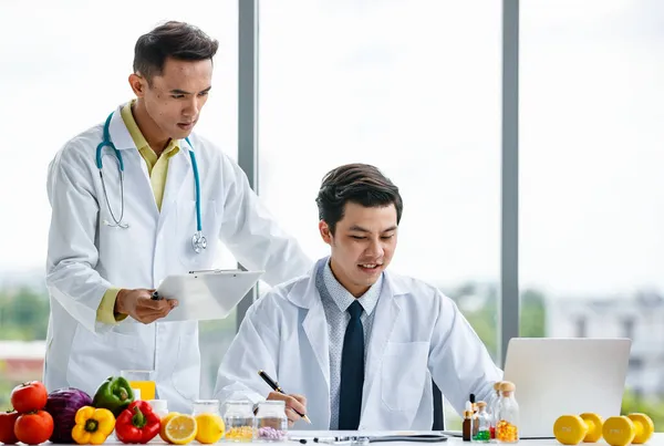Üniformalı Asyalı Erkek Doktorlar Klinikte Birlikte Çalışırken Meyve Vitaminlerin Yanındaki — Stok fotoğraf