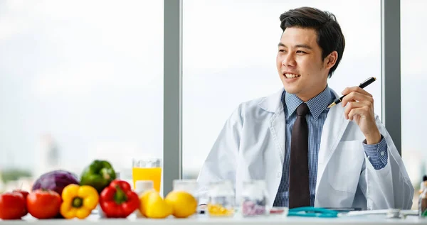 若くて見栄えの良い医療従事者の肖像現代のクリニックのオフィスで健康的な食べ物と机の上に座って — ストック写真