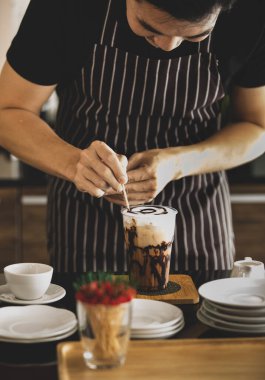 Barista, sütlü buzlu kahveyi dikkatlice süslemek için kürdan kullanarak üzerine örümcek ağı gibi çikolata desenleri çizerek sarhoş olmanın daha çekici görünmesini sağlıyor..
