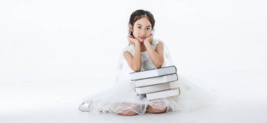 Asyalı güzel kızın portresi beyaz prenses çiçekli elbise giyer. Beyaz arka planda bir yığın kitapla poz verir..