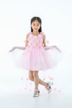 Küçük Asyalı şirin balerin çocuğun portresi. Yüksek topuklu güzel bale elbisesi içinde. Beyaz arka planda gülümseyerek zarif bir jest yapıyor..