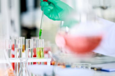 Kimliği belirsiz bir bilim adamı laboratuarda kimyasal araştırmalar yaparken cam test tüpüne yeşil sıvı döküyor..