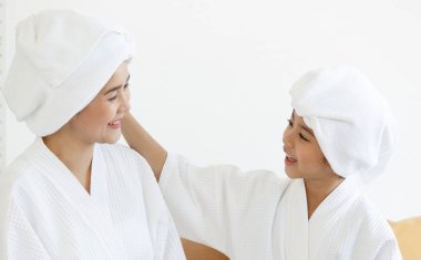 Anne ve kızı spa elbisesi giyip başları havluyla örtülü ve beyaz elbiseli bir kaplıcada mutlulukla konuşup dalga geçiyorlar. Sağlık ve rahatlama ve aile ilişkileri hakkında fikir.