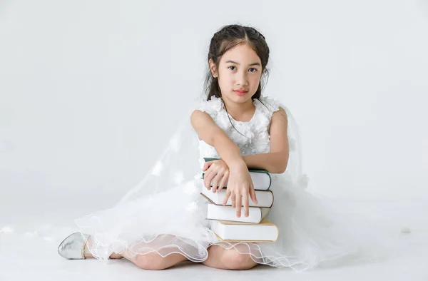 ポートレートスタジオショットのアジアの可愛いです女の子身に着けていますホワイトプリンセス長いバラの花のドレスファッション衣装ポージングとともに本のスタック上の白い背景 — ストック写真