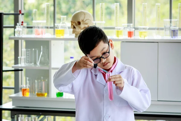 在现代学校实验室进行科学研究时 认真的亚洲男孩穿着实验室外套 戴着水滴管混合五颜六色试剂的眼镜 — 图库照片