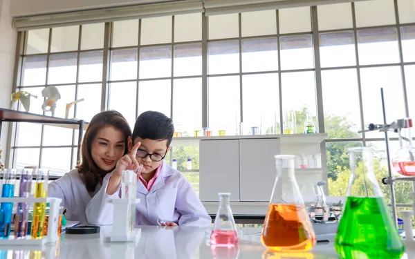 カラフルな液体を混合しながら 実験室で化学の授業中に講師の助けを借りて実験を行うアジアの少年に焦点を当て — ストック写真