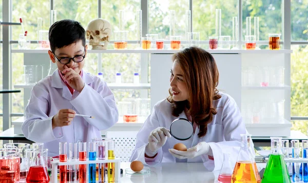 化学実験室で科学実験中にカラフルな液体を混合しながら 鶏の卵を検討拡大鏡を持つ若いアジアの女性 — ストック写真