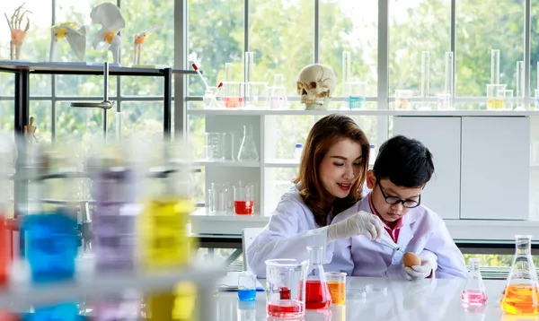 在实验室化学课上 在导师的帮助下进行实验时 亚洲学生混合了五颜六色的液体 — 图库照片