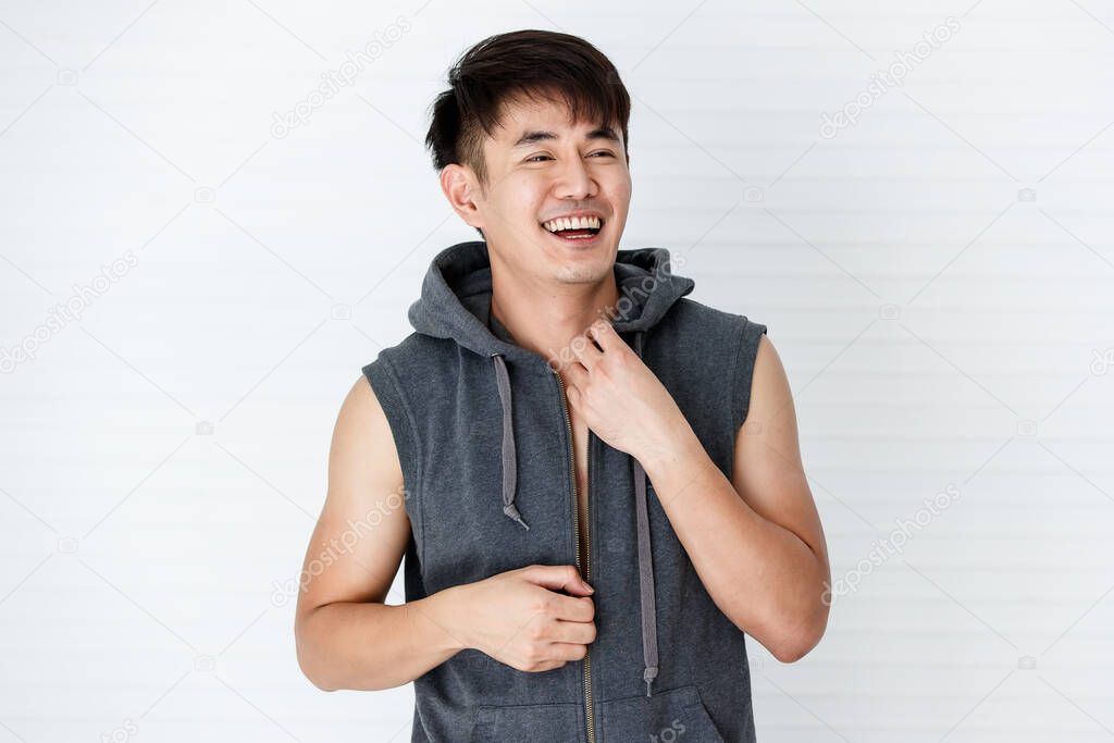Asain handsome smiling man wearing sportsware sleeveless gray T-shirt good mood happy holding hand a shirt on a white bacjground