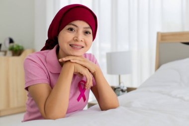 Memnuniyetle pembe tişörtlü Asyalı kadın ve hastanede göğüs kanseri hastası olarak başını kırmızı eşarpla örtmesi güven ve yüzle gülümsemesi..