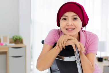 Memnuniyetle pembe tişörtlü Asyalı kadın ve hastanede göğüs kanseri hastası olarak başını kırmızı eşarpla örtmesi güven ve yüzle gülümsemesi..