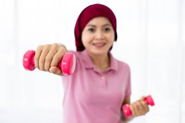 Neşeli Asyalı kadın kanser hastasının ellerinden tutulan pembe plastik halterden canlı kesim ve hastalıklara karşı güçlü bir sağlık ve moral tazeleme aracı.