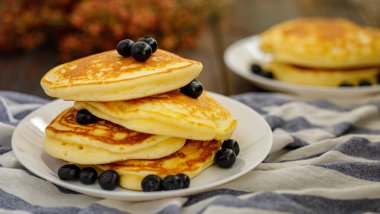 Lezzetli krep yığını yaban mersini ve kuru yapraklı tatlı yemek, ahşap arka planda beyaz tabakta ekose kumaş