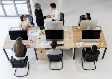 Patron adamı tebrik ediyor ve onunla tokalaşıyor. Ekip modern ofiste çalışmaya odaklanmış, neşeli ve başarıya şükrediyor..