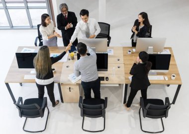 Patron ve meslektaşları takımdaki adamı tebrik ediyor ve tokalaşıyorlar. Başarılı oldukları için mutlular. Beyaz arka planda modern ofis.