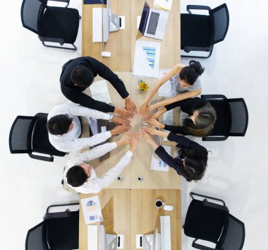 Profesyonel iş analiz ekibi takım çalışması sembolü olarak el ele verdi, modern bilgisayarların çalışma masası ve kağıt grafiklerinin arka planı, üst görünüm.