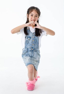 Portre, Asyalı, kot pantolonlu, kot etekli, gülümseyen kameraya gülümseyen, kalp şeklinde el ele tutuşan küçük tatlı bir kızın izole edilmiş bir fotoğrafını çek..