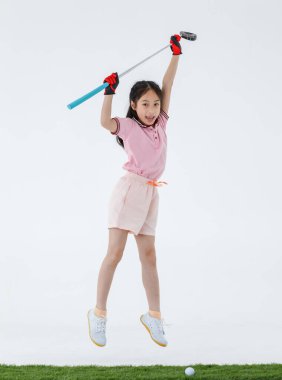 Spor formalı mutlu Asyalı golfçünün izole edilmiş bir fotoğrafı yeşil çimlerin üzerinde duruyor golf sopası sürücüsünü ellerinde neşeli bir şekilde beyaz arka plan önünde gülüyor gibi yapıyor..