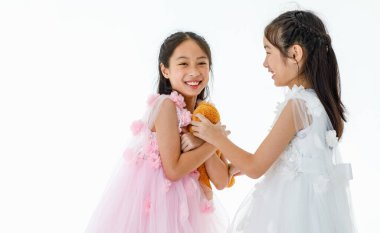 Portre, iki küçük Asyalı balerin, pembe ve beyaz güller içinde bale elbisesi giyip turuncu oyuncak ayı bebeği için gülerken çekilmiş..