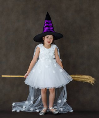 Beyaz cadı kostümlü, siyah mor şapkalı, elinde turuncu balkabağı suratlı, sihirli süpürge sopası olan Asyalı bir çocuğun portresi..