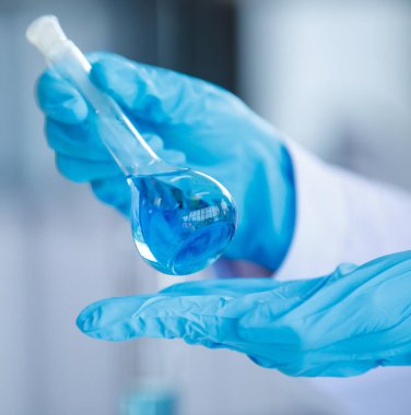 Plastik eldiven arka planında, analistin elinde mavi sıvı bulunan el laboratuarı deney şişesini kapat. Kavram Bilimi deneyi
