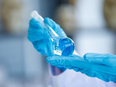 Plastik eldiven arka planında, analistin elinde mavi sıvı bulunan el laboratuarı deney şişesini kapat. Kavram Bilimi deneyi