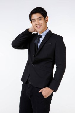 Asyalı genç, kısa saçlı, zeki, kendine güvenen iş adamı resmi takım elbiseli, gülümseyen ellerini cebinde tut ve beyaz arka plandaki kameraya bak..