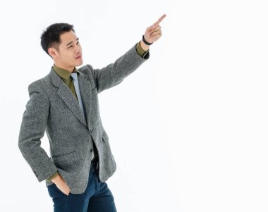 Kısa siyah saçlı, zeytin yeşili tişörtlü, gri kravatlı, koyu gri takım elbiseli, ayakta duran, sol üst taraftan sol elini gösteren, sağ elini beyaz arka planı olan pantolonunun cebine sokan adam. Harika bir yere işaret ediyor.