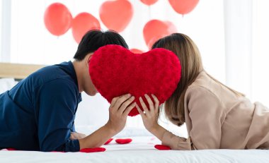 Sevgililer Günü 'nde, kırmızı kalp şeklindeki yastığın arkasına saklanan isimsiz bir adam ve kadının yan görüntüsü.