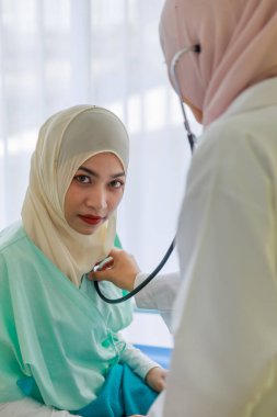 Genç kadın müslüman doktor hastanede steteskopla Müslüman hastanın kalbini kontrol ediyor..