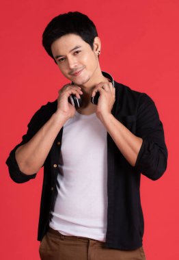 Yakışıklı, gülümseyen Asyalı adam kulaklıkları boynunun iki tarafından alıyor. Ve ağzının köşesinde gülümse Kırmızı arka plan Eğlence konsepti