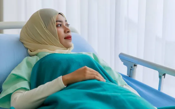 病気の若い女性の肖像アジアのイスラム教徒の患者は 患者のガウンを着て病院のベッドの上に横たわっていると病院の窓の外を見て緑の毛布でカバー — ストック写真