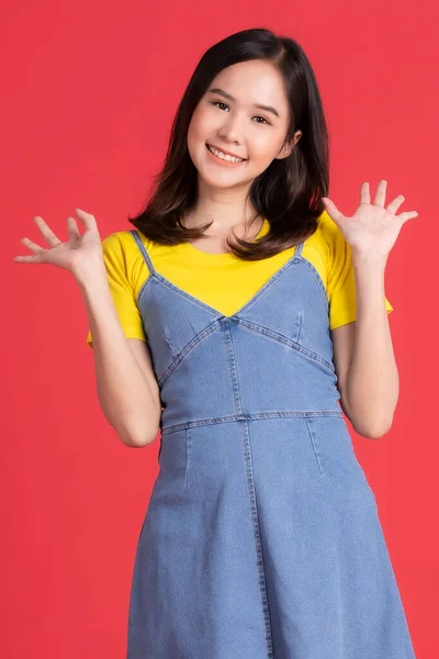 アジアの女の子赤い背景に優しい笑顔で商品やコンテンツジェスチャーを広告やプレゼンテーションで黄色のシャツと短いスカートポーズを身に着けています — ストック写真