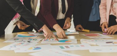 Tanımlanamayan iş kadınlarının bir araya geldiği bir grup çalışma masasında beyin fırtınası yapıyorlar, parmaklarını ve analiz veri tablosunu gösteriyorlar ve özgüvenle grafiklerini çiziyorlar ve takım halinde bilgi alışverişi yapıyorlar..