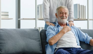 Beyaz, yaşlı, yaşlı, yaşlı, gri sakallı ve koltukta oturan kocanın sırt ağrısı çeken bir omuz ağrısı çekerken bakım eşinin sırt masajı yaparken çekilmiş yakın çekimi..