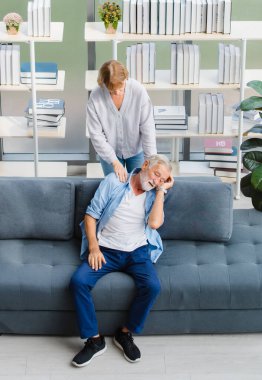 Güzel, beyaz, yaşlı, yaşlı bir eş, masaj yaparken mutlu beyaz saçlar ve sakallı koca omuz, oturma odasındaki rahat koltukta dinleniyor, kitaplığın ve ağaç kabının önünde..