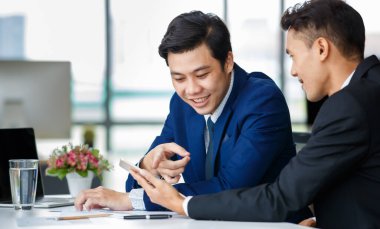 Memnuniyetle Asyalı erkek yöneticiler masada oturup birlikte tablet kullanırken işyerindeki yeni projeden bahsediyorlar.