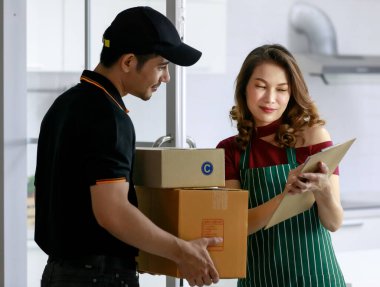 Asyalı kurye teslimat kağıdını imzalayan Asyalı bayan dükkan sahibine posta paketi teslim ediyor. Kapıdan kapıya nakliye, E-ticaret sektörü konsepti