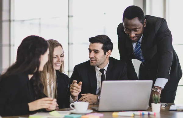 オフィスワークテーブルに座っている間にノートパソコンの前に集まった集中的な白人の同僚との専門的な大人のアフリカのビジネスマンの指導者のポインティングとコンサルティング計画戦略 — ストック写真