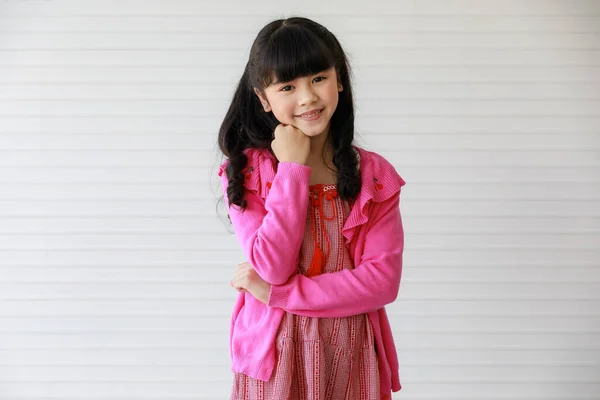 穿着粉色衣服的可爱可爱而快乐的亚洲小女孩 快乐地微笑着 摆出姿势 用手托着下巴创造性地思考或做梦 站在那里看着相机 — 图库照片