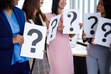 Tanımlanamayan, kimliği belirsiz, takım elbiseli kadın memurun stüdyo fotoğrafı beyaz arka planda cevapları şüpheli olan soru işareti kağıdının çeşitli yazı tiplerini tutuyor..