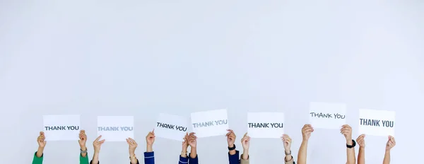 さまざまなフォントのスタジオショット白い背景に顧客への感謝を示す認識できない顔のない役員のスタッフのグループによって頭の上に保持された文字の紙のサインに感謝 — ストック写真