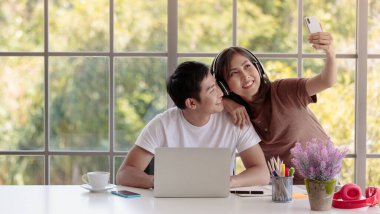 Genç ve çekici Asyalı çift oturma odasında cam pencereli bir selfie çekiyorlar. Aşk ve çift ilişkisi kavramı.